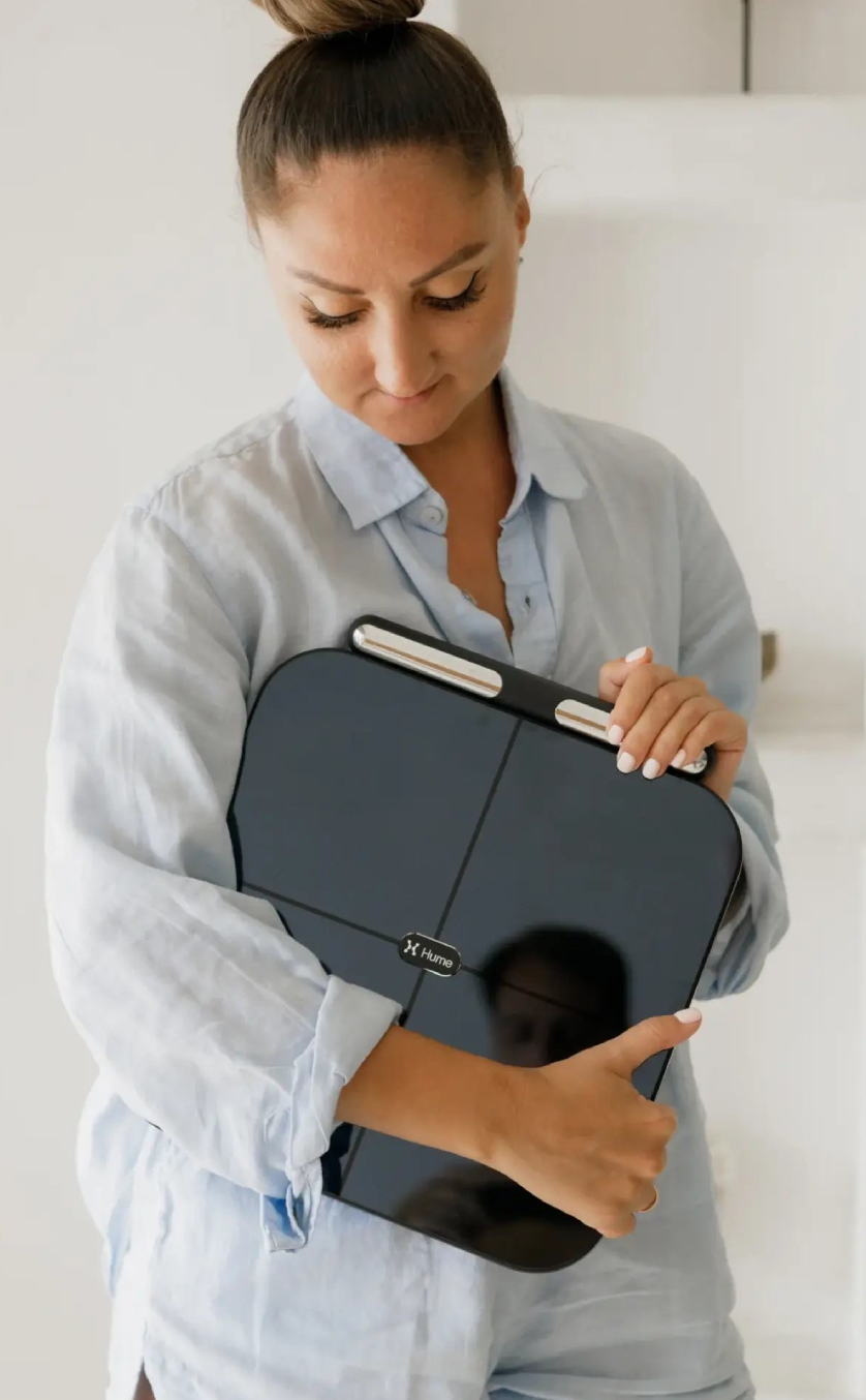 Woman holding a Hume Pod scale in her arms, showcasing a sleek smart body composition device for tracking weight, body fat, and muscle mass.